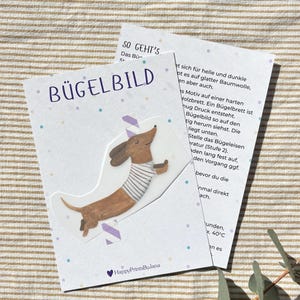 Könnte beinhalten: Eine Karte mit einem Bügelbild eines Dackels. Der Dackel ist braun und trägt ein gestreiftes Shirt. Auf der Karte steht das Wort "BÜGELBILD" und Text. Dekoriert mit kleinen blauen und lila Punkten.