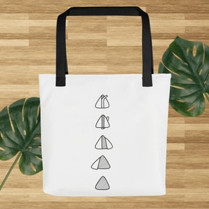 May include: White tote bag with black handles and a design of five black and white onigiri, a Japanese rice ball.