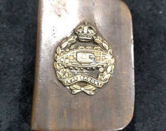 Puede incluir: Una caja de bolsillo de metal dorado con una cresta real y un emblema de tanque. El emblema dice "Fear Naught".