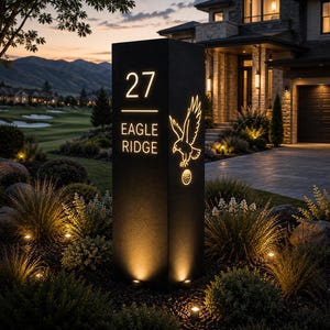 Può includere: Un alto pilastro nero rettangolare per indirizzi con testo ritagliato illuminato che recita 27 EAGLE RIDGE. Il design include la sagoma luminosa di un'aquila in volo sopra una pallina da golf. Il pilastro è posizionato all'aperto al crepuscolo.