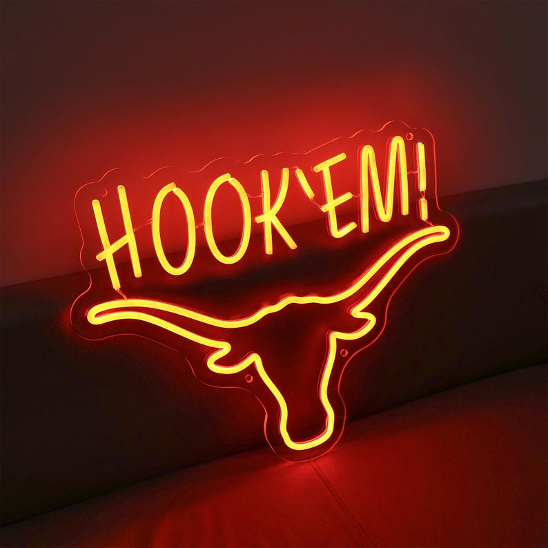 May include: Neon sign with a yellow "HOOK'EM!" text and a red longhorn steer silhouette.