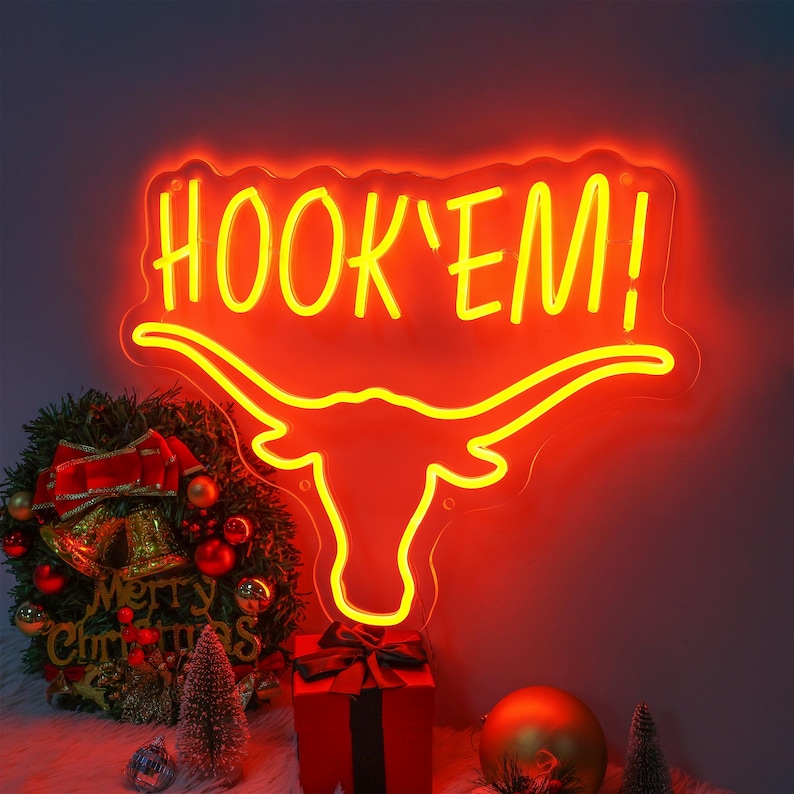 May include: A neon sign with a yellow "HOOK'EM!" text and a red longhorn steer silhouette. The sign is lit up and has a red glow.