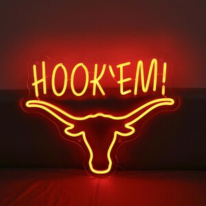May include: Neon sign with a yellow "HOOK'EM!" text and a red longhorn steer silhouette.