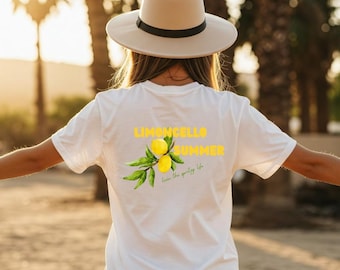 May include: A white t-shirt with a yellow "Limoncello Summer" graphic and a lemon and leaf illustration. The shirt also has the text "live the spritely life". A person is wearing a beige hat.