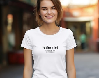 May include: A white short-sleeved t-shirt featuring the black printed text "millennial" followed by "DÜSSELDORF 2026" and "ICH WAR DABEI" centred on the chest. The garment has a round neckline and a standard fit, constructed from plain white fabric.