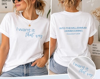 Pode incluir: Uma t-shirt branca de manga curta com texto em azul claro. A frente apresenta a frase I want it that way. As costas exibem o texto INTO THE MILLENNIUM HOMECOMING Düsseldorf 2026. A peça é feita de tecido branco com gola redonda.