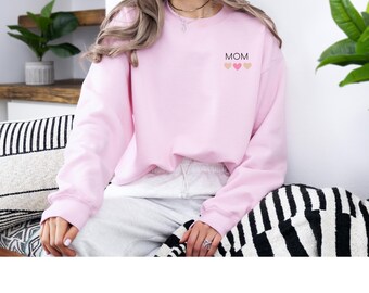 May include: A pink sweatshirt with the word "MOM" and three small hearts in pink, peach, and brown on the front.