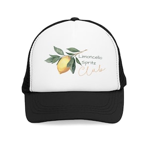 Könnte beinhalten: Schwarze und weiße Trucker-Mütze mit weißer Frontplatte. Auf der Vorderseite befindet sich eine Aquarellillustration einer Zitrone und Blättern mit dem Text "Limoncello Spritz Club" in goldener Schrift.