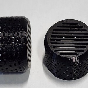 May include: Two black plastic cylindrical air filters with different designs. One filter has a grid pattern and the other has a series of small holes.