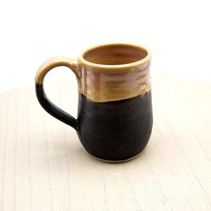 May include: A black and brown ceramic mug with a rounded shape and a handle. The mug has a glazed finish.
