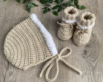 May include: A crocheted baby hat and booties set in a beige color with a white fur trim. The hat has a tie at the bottom.