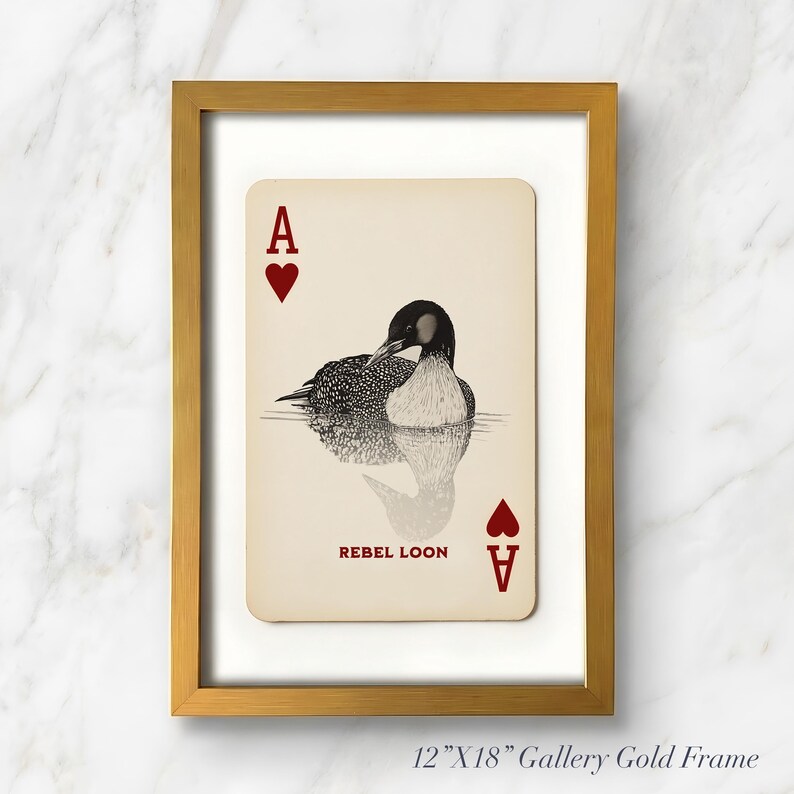 Puede incluir: Una impresi&oacute;n enmarcada con un dise&ntilde;o de carta de As de Corazones con una ilustraci&oacute;n en blanco y negro de un colimbo en el agua. La carta incluye el texto REBEL LOON en rojo. La obra est&aacute; en un marco dorado de 30,48 cm por 45,72 cm.