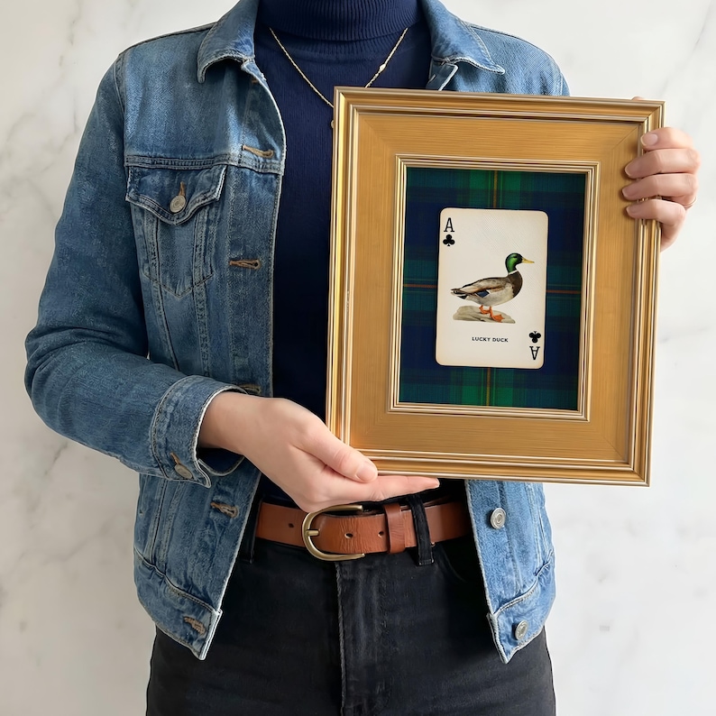 May include: A framed playing card featuring an illustration of a duck, labeled "Lucky Duck." The card is set against a green and blue plaid background within a gold-colored frame. The frame is rectangular.