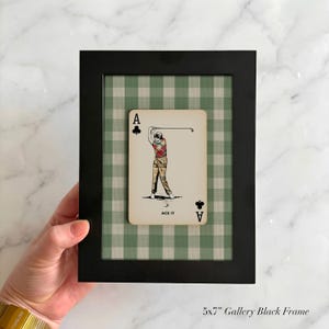 K&ouml;nnte beinhalten: Ein 13x18 cm gro&szlig;er schwarzer Galerierahmen mit einer Spielkarte, die einen Golfspieler beim Abschlag zeigt. Die Karte tr&auml;gt den Text ACE IT und den Buchstaben A mit einem Kreuz-Symbol. Der Hintergrund im Rahmen hat ein gr&uuml;nes Vichy-Muster.