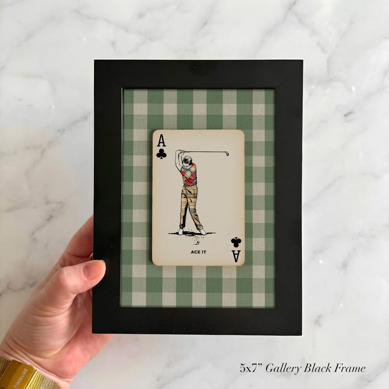 K&ouml;nnte beinhalten: Ein 13x18 cm gro&szlig;er schwarzer Galerierahmen mit einer Spielkarte, die einen Golfspieler beim Abschlag zeigt. Die Karte tr&auml;gt den Text ACE IT und den Buchstaben A mit einem Kreuz-Symbol. Der Hintergrund im Rahmen hat ein gr&uuml;nes Vichy-Muster.