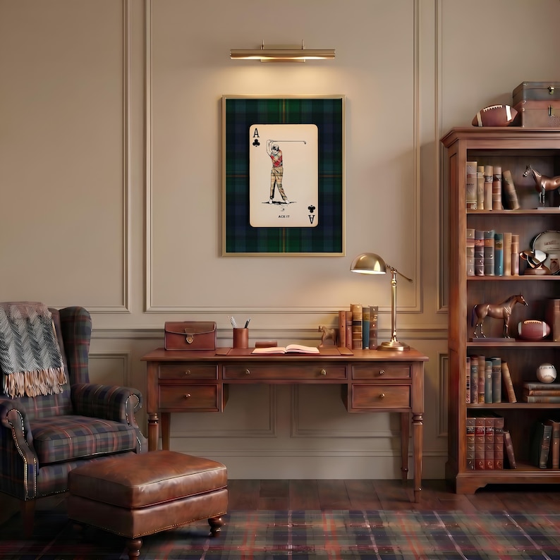 May include: A framed Ace of Clubs playing card featuring a golfer, set against a green and blue plaid background. The room includes a wooden desk, a bookshelf, a plaid armchair, and a leather ottoman, creating a classic, cozy aesthetic.