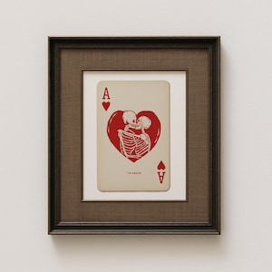Pode incluir: Impressão artística emoldurada com um design de carta de baralho. A carta é o Ás de Copas, com um coração vermelho contendo dois esqueletos se beijando. O texto "'Til Death" está abaixo do coração. A moldura é marrom escuro.