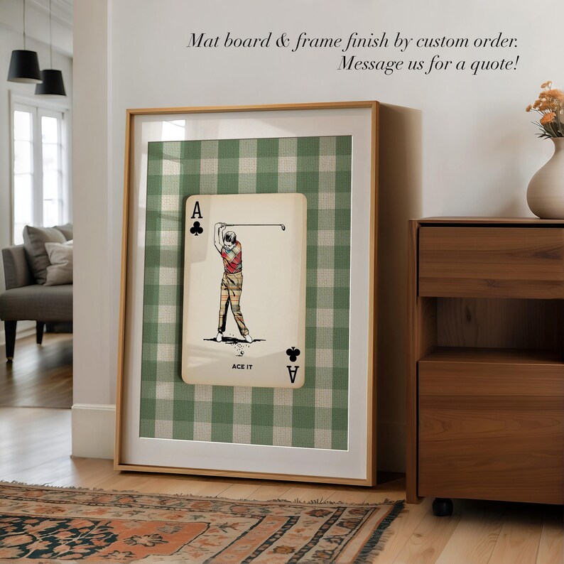 K&ouml;nnte beinhalten: Ein gerahmter Kunstdruck mit einem Kreuz-Ass-Spielkartendesign, einer Golfspieler-Illustration und dem Text ACE IT. Der Druck ist vor einem gr&uuml;n-wei&szlig;en Vichy-Karo-Hintergrund platziert und befindet sich in einem hellen Holzrahmen.