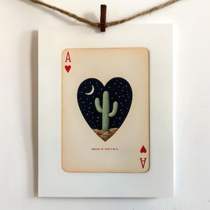 May include: Ace of Hearts playing card art print. The card features a heart-shaped design with a night sky, cactus, and crescent moon. The text "MADE IN THE U.S.A." is printed at the bottom.