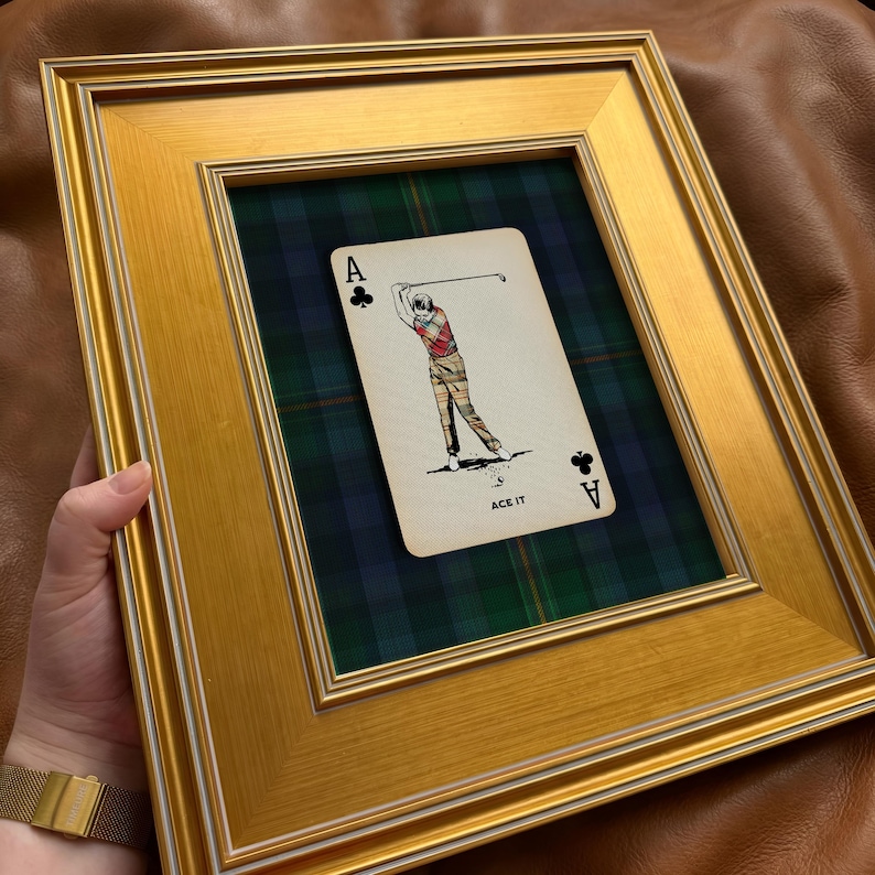 May include: Gold framed artwork featuring a playing card with a golf theme. The card shows a golfer in action, set against a green and blue plaid background. The card reads "ACE IT".