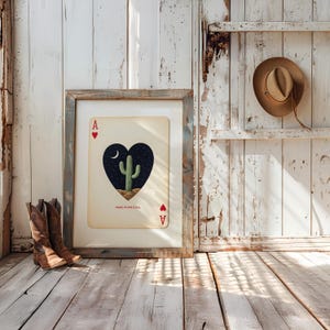 May include: Framed Ace of Hearts playing card art featuring a cactus under a starry night sky. The card is framed in a rustic, weathered wood frame. The text "MADE IN THE U.S.A." is visible. Brown cowboy boots are in the foreground.