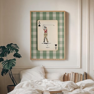 K&ouml;nnte beinhalten: Ein rechteckiger Wandkunstdruck mit einer cremefarbenen Spielkarte, einem Kreuz-Symbol und dem Text ACE IT. Die Karte zeigt die Illustration eines Golfers, der einen Schl&auml;ger schwingt. Der Hintergrund ist ein gr&uuml;n-wei&szlig;es Vichy-Muster.