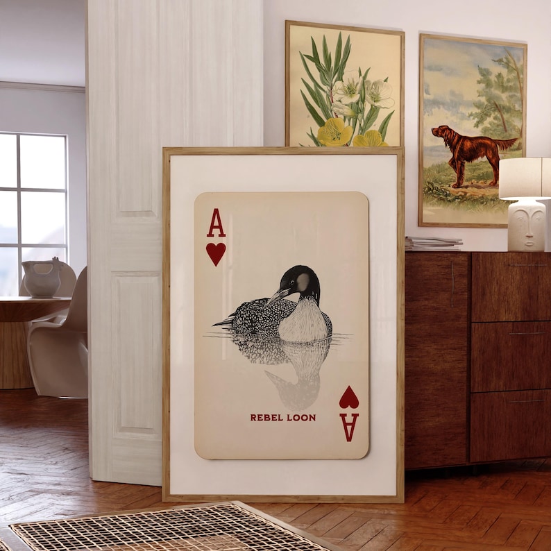 Puede incluir: Una l&aacute;mina de arte enmarcada con un dise&ntilde;o de carta de juego sobre fondo crema, con un s&iacute;mbolo de coraz&oacute;n rojo y la letra A en las esquinas. El centro muestra una ilustraci&oacute;n detallada en blanco y negro de un colimbo con el texto REBEL LOON.