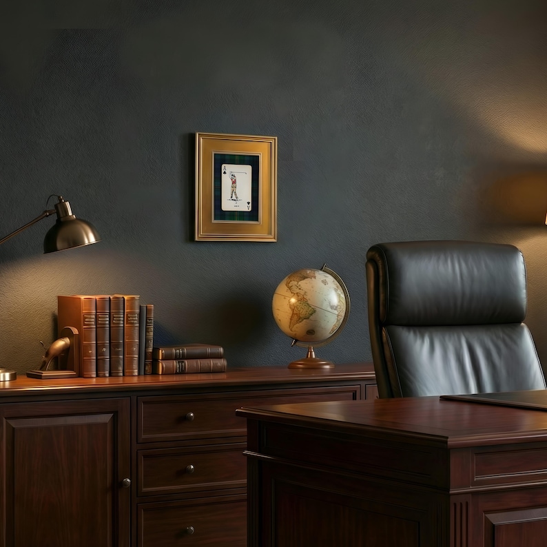 May include: A framed playing card featuring a golfer, displayed on a dark wall. The gold frame surrounds the card, which is set against a green and blue plaid background. The scene includes a desk, books, a globe, and a leather chair.