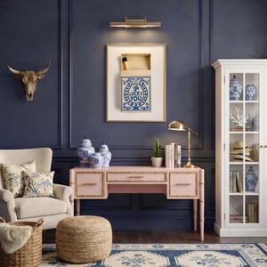 May include: A home office with a pink desk, gold accents, and blue and white decor. A framed artwork with the text "LUCKY YOU" hangs above the desk. A white cabinet displays decorative items. A cow skull and a reading lamp are also visible.
