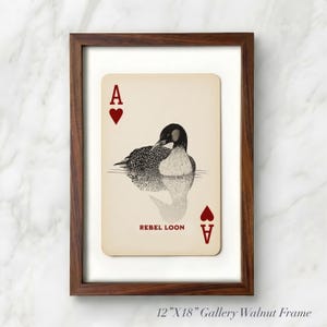 Puede incluir: Una impresi&oacute;n enmarcada de 30,48 cm x 45,72 cm con un dise&ntilde;o de carta de juego que muestra una ilustraci&oacute;n en blanco y negro de un colimbo en el agua. La carta tiene fondo crema, corazones rojos, la letra A en las esquinas y el texto REBEL LOON.