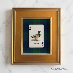 May include: A framed playing card featuring a duck illustration, labeled "Lucky Duck," set against a plaid background. The card is framed in a gold beveled frame, creating a decorative wall art piece.