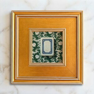 A gold framed mini painting print of a white dragon mahjong tile set against a green and white chinoiserie background. Print is 5x5" and gold frame is 3.5" making the finished size 10.5"x10.5". Art is styled with a soft white marble background.