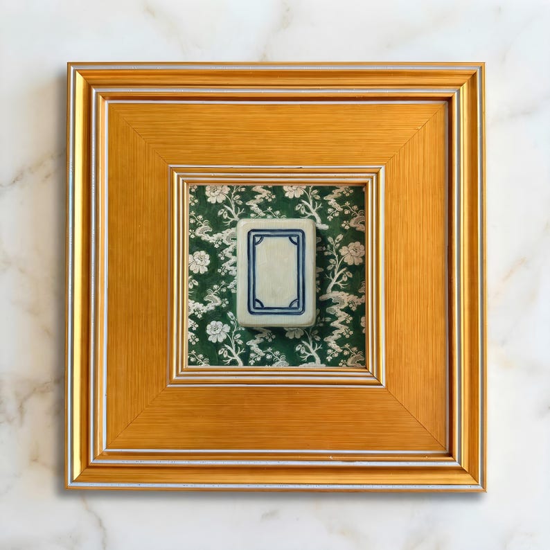 A gold framed mini painting print of a white dragon mahjong tile set against a green and white chinoiserie background. Print is 5x5" and gold frame is 3.5" making the finished size 10.5"x10.5". Art is styled with a soft white marble background.