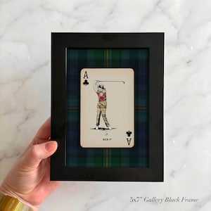 May include: Black framed art piece featuring an Ace of Clubs playing card with a golfer illustration. The card is set against a plaid background of green, blue, and black. The frame is labeled "5x7" Gallery Black Frame."