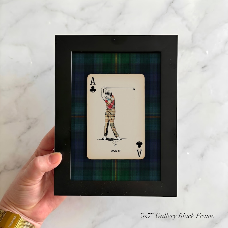 May include: Black framed art piece featuring an Ace of Clubs playing card with a golfer illustration. The card is set against a plaid background of green, blue, and black. The frame is labeled "5x7" Gallery Black Frame."