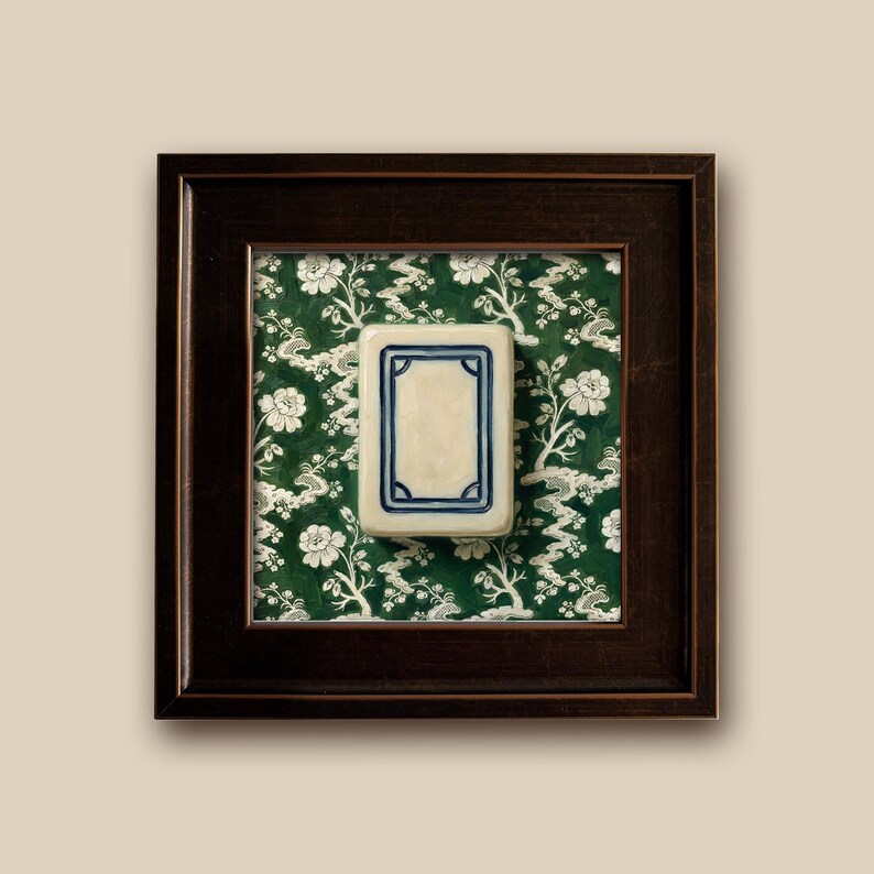 A framed piece featuring a rectangular White Dragon Mahjong tile with a cream-colored center and a blue border. The tile is set against a green floral chinoiserie patterned background and enclosed in a dark brown wooden frame. The artwork is displayed on a neutral-colored wall. Print is 5x5" Slimwood Black-Gold frame is .85" Finished size is 6.5"x6.5"