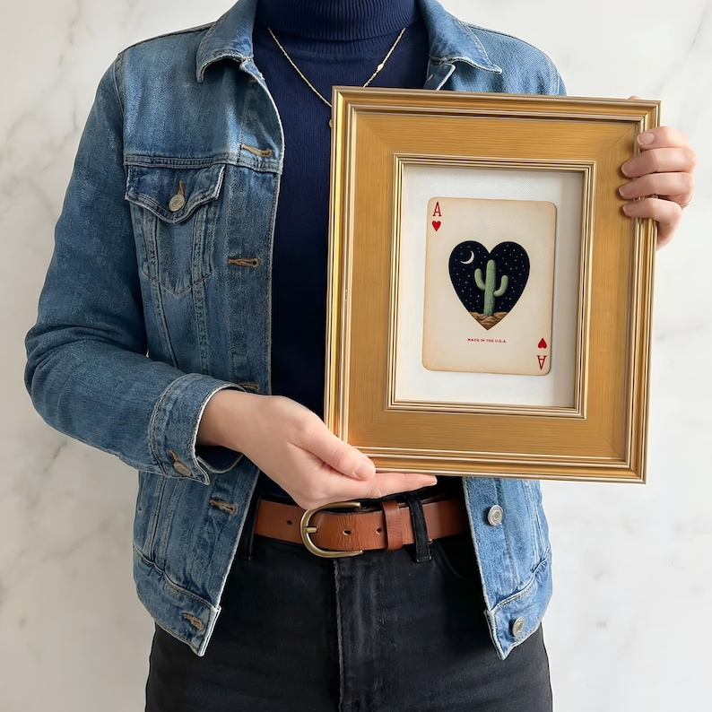 May include: A framed playing card featuring a heart-shaped design with a cactus, moon, and stars. The card is an Ace of Hearts, set in a gold-colored frame. The text "MADE IN THE U.S.A." is visible on the card.