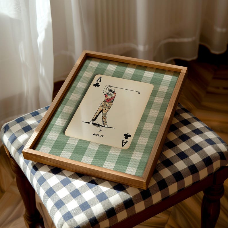 K&ouml;nnte beinhalten: Ein gerahmter Druck mit einem Kreuz-Ass-Spielkartendesign, einer Golfspieler-Illustration und dem Text ACE IT. Der Druck ist vor einem gr&uuml;n-wei&szlig;en Vichy-Karo-Hintergrund platziert und in einem hellen Holzrahmen mit sauberer Kante eingefasst.