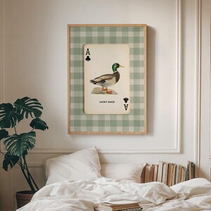 May include: A rectangular wall art print featuring a playing card design with a mallard duck illustration. The card displays the text LUCKY DUCK, an ace of clubs symbol, and is set against a light green and white gingham checkered background.