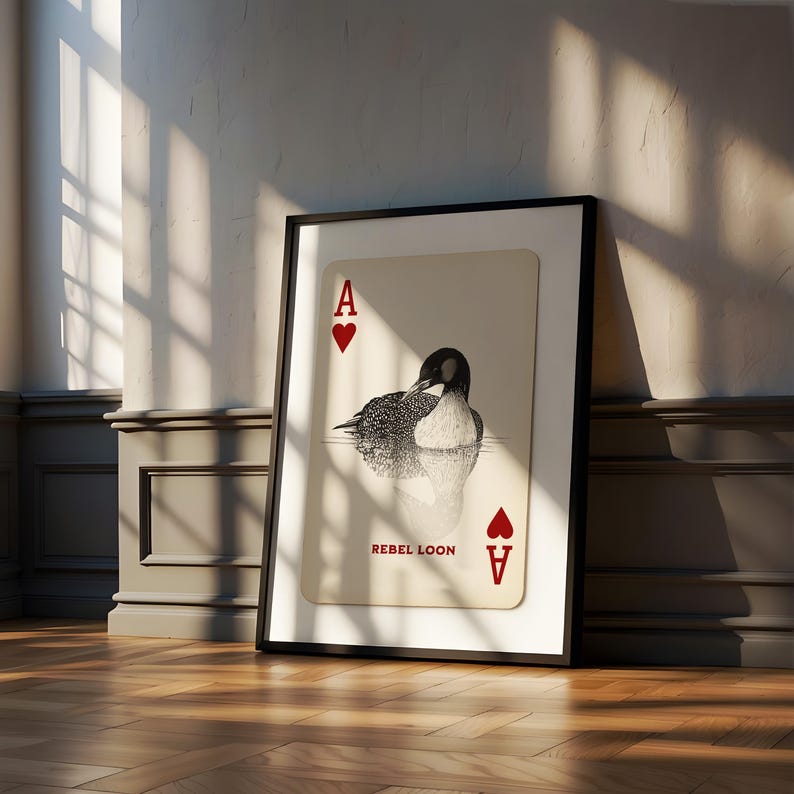 Puede incluir: Una l&aacute;mina enmarcada con un dise&ntilde;o de carta de juego sobre fondo crema, una ilustraci&oacute;n en blanco y negro de un colimbo, corazones rojos en las esquinas, la letra A y el texto REBEL LOON impreso en rojo en la parte inferior.
