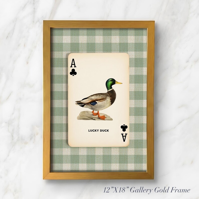 May include: A framed wall art piece featuring a playing card design with a mallard duck illustration, the text LUCKY DUCK, and club symbols. The card is set against a green and white gingham background inside a 12-inch by 18-inch gold frame.