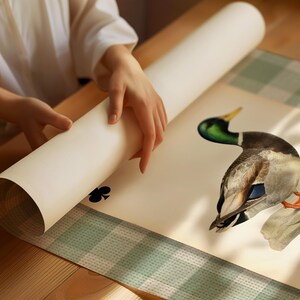 May include: A rolled-up poster featuring a detailed illustration of a mallard duck with a green head and brown body, accompanied by a black club playing card symbol printed on a cream-colored background, partially unrolled on a green checkered surface.
