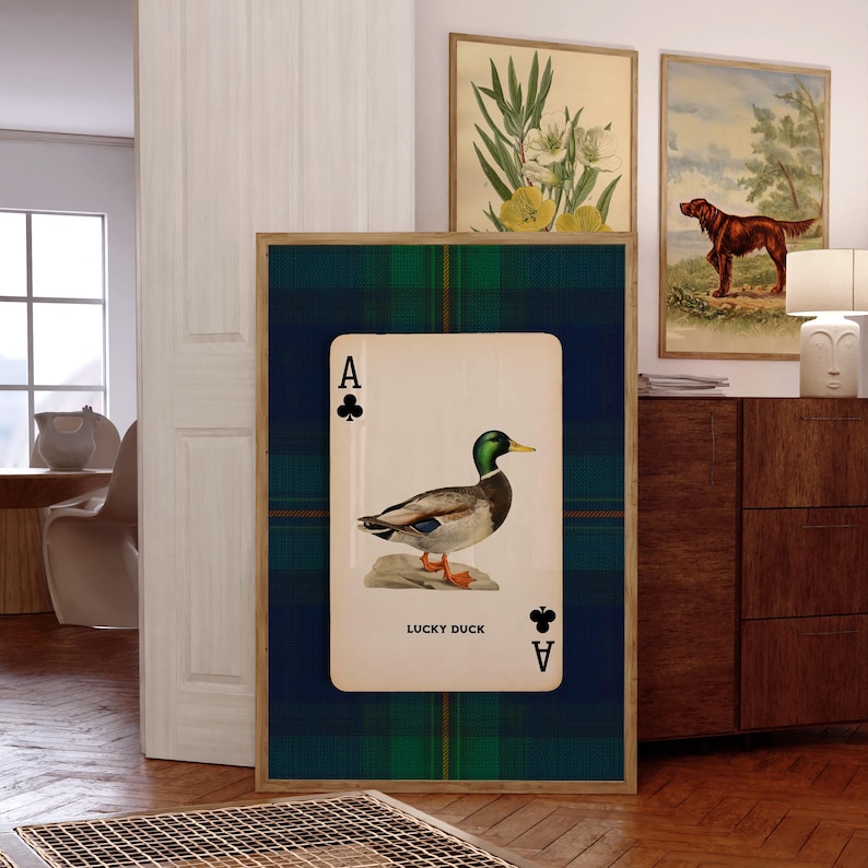 May include: Framed wall art featuring a playing card design with a duck illustration. The card is the Ace of Clubs, with the words "LUCKY DUCK" printed below the duck. The background is a green and blue plaid pattern.