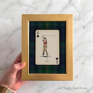 May include: A gold framed print featuring a playing card with a golfer illustration. The card is set against a green and blue plaid background. The card reads "ACE IT" and has the Ace of Clubs and Ace of Spades symbols.