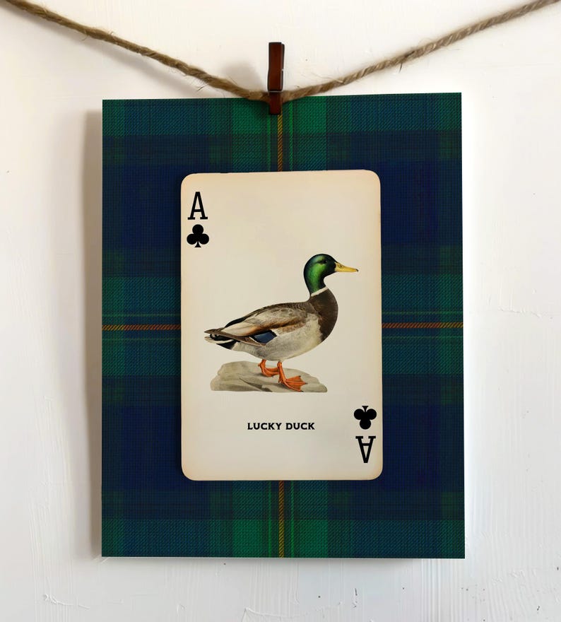 May include: A framed print featuring an Ace of Clubs playing card with a duck illustration. The card is centered on a green and blue plaid background. The text "LUCKY DUCK" is below the duck image.