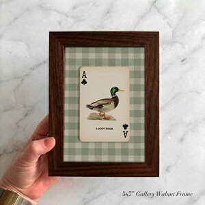 May include: A 5x7 inch dark walnut wood frame containing a playing card with an illustration of a mallard duck. The card features the text 'A' and club symbols in the corners, with 'LUCKY DUCK' printed below the duck on a green gingham background.