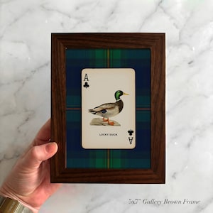 May include: A framed playing card featuring a duck illustration, labeled "Lucky Duck," set against a blue and green plaid background. The frame is a dark brown color. The text "5x7" Gallery Brown Frame" is at the bottom.