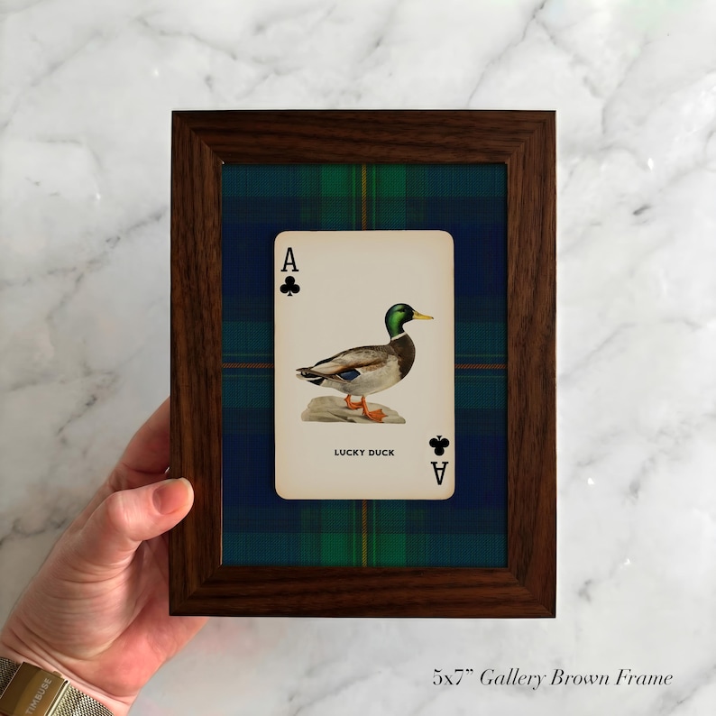 May include: A framed playing card featuring a duck illustration, labeled "Lucky Duck," set against a blue and green plaid background. The frame is a dark brown color. The text "5x7" Gallery Brown Frame" is at the bottom.