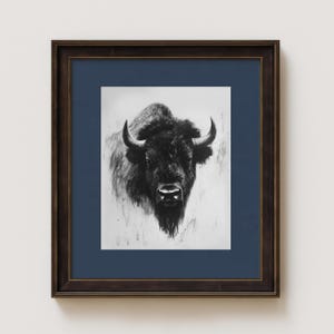 May include: Black and white print of a bison, framed in a dark brown wooden frame with a navy blue mat. The bison is centered, with detailed fur and prominent horns. The artwork is a portrait style.