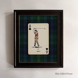 May include: Framed artwork featuring a playing card design. The card is the Ace of Clubs, with an illustration of a golfer in action. The background is a green and blue plaid pattern, and the frame is black. The text "ACE IT" is at the bottom of the card.